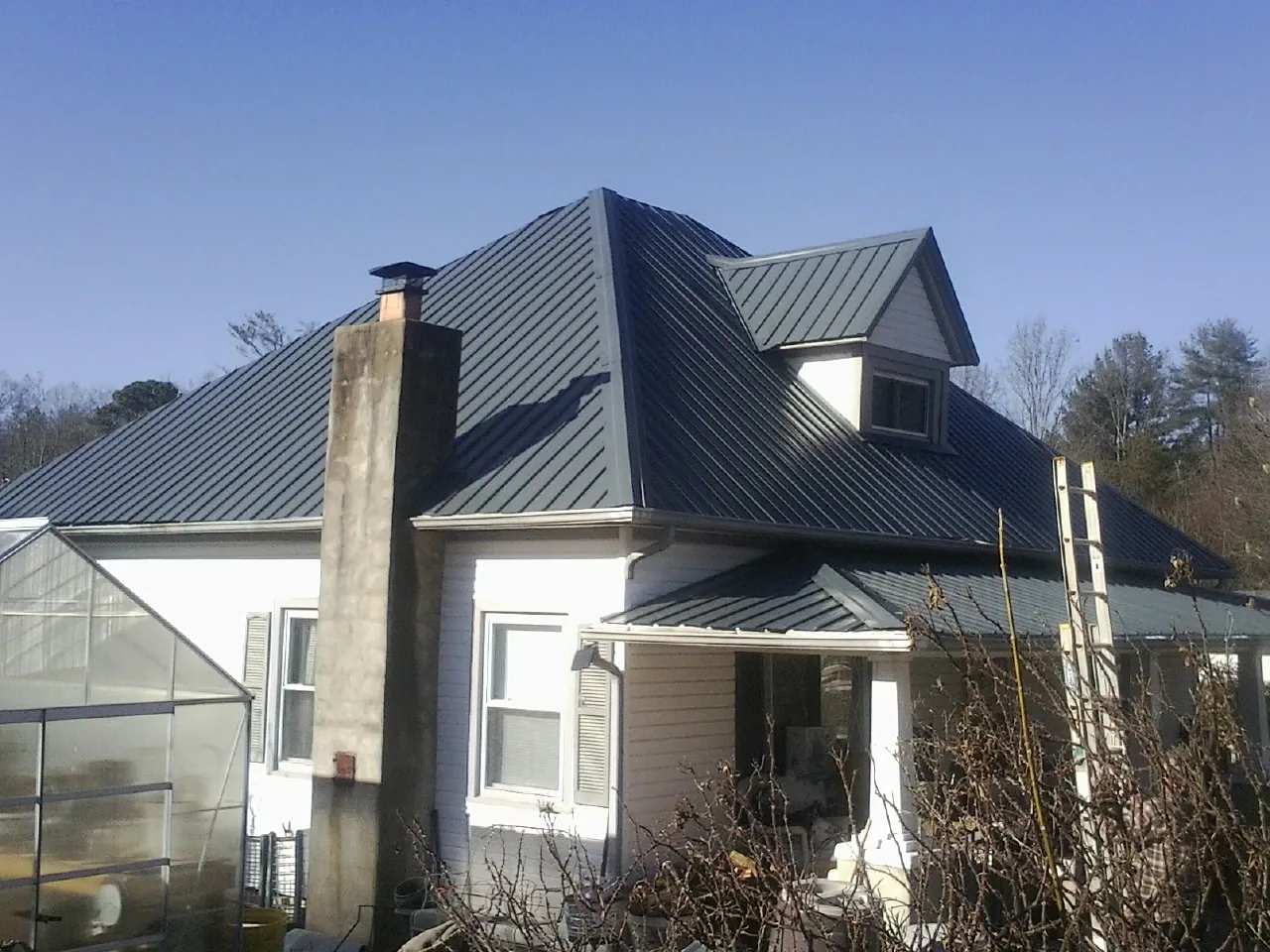 Dark blue standing seam metal roof on a white farmhouse with dormer — Slate & Tile Roof Repair by Roofing Brothers in Denton