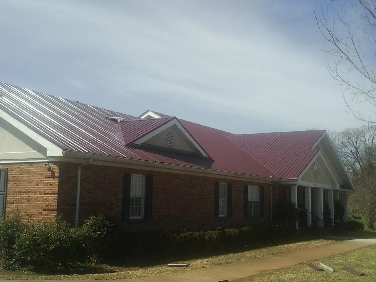 Red metal roof with gabled entries on a long brick building, from a Hail Damage Roof Repair job in Denton