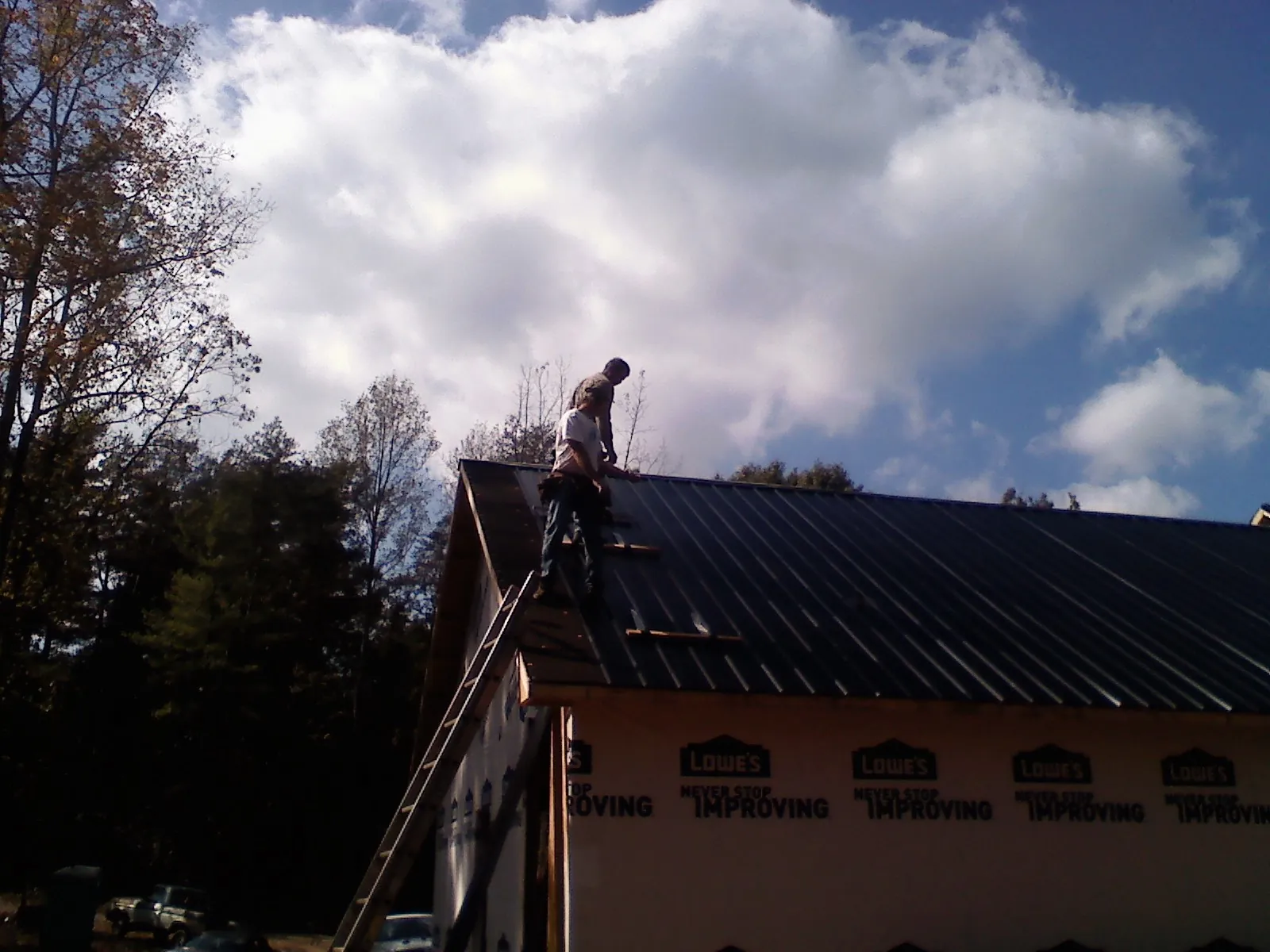 Roofer fastening dark metal panels high against a cloudy sky, from a Roof Inspection job in Denton