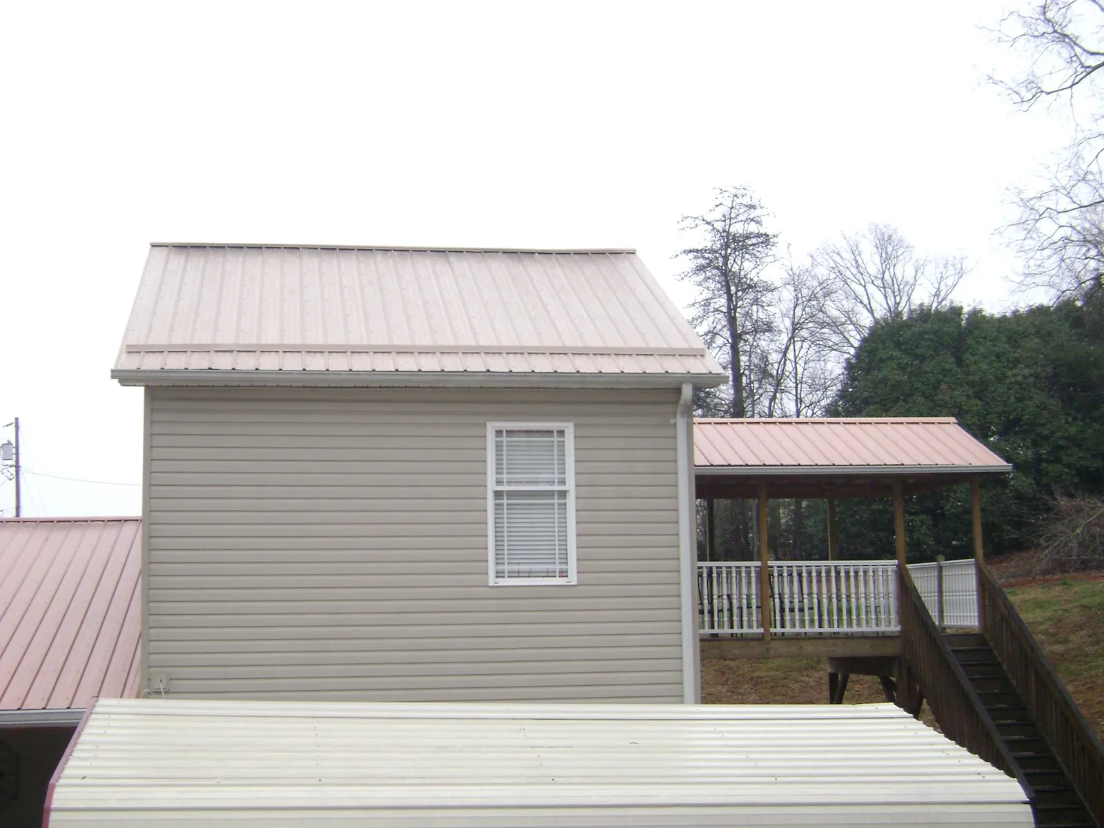Tan metal roofs on a two story addition and attached porch, from a Roof Replacement job in Denton